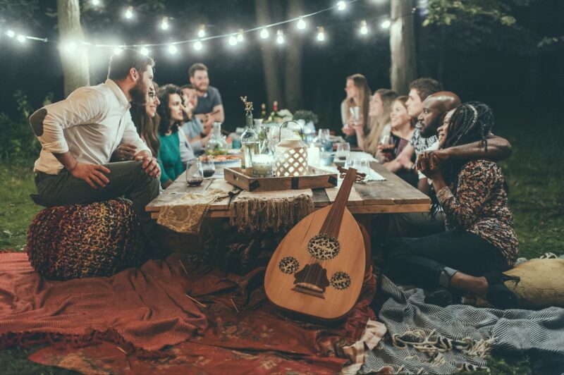Friends having an evening picnic under fairy lights at a long table